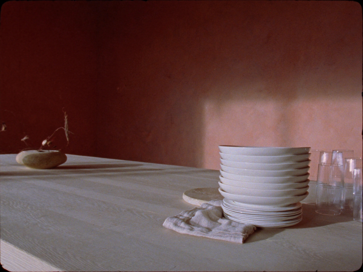 A pale oak table set with chalk-white stoneware, glass tumblers and a travertine board in a warm clay-plaster room