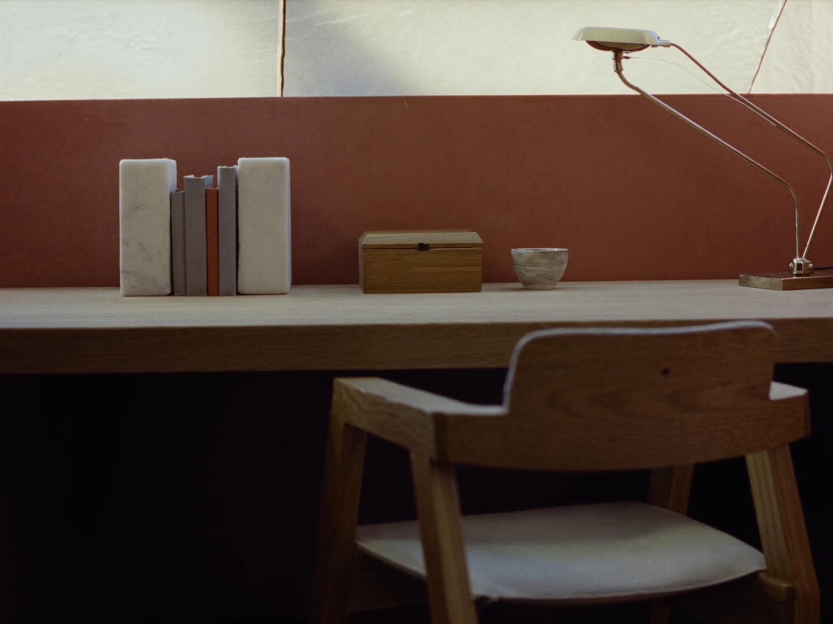 Marble bookends, a timber box and a brass desk lamp on a pale shelf against warm plaster
