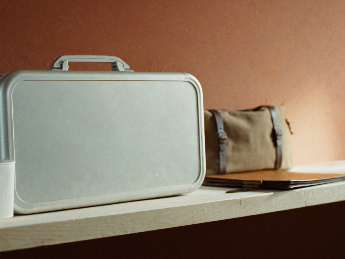 Plain aluminium travel case, waxed canvas holdall and leather document folio on a pale oak bench